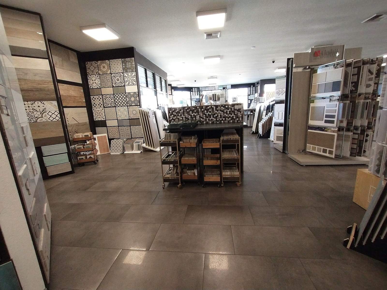 Tegelwinkel met wanden vol tegelstalen in houtlook, cementtegels en mozaïek, met karretjes vol monsters