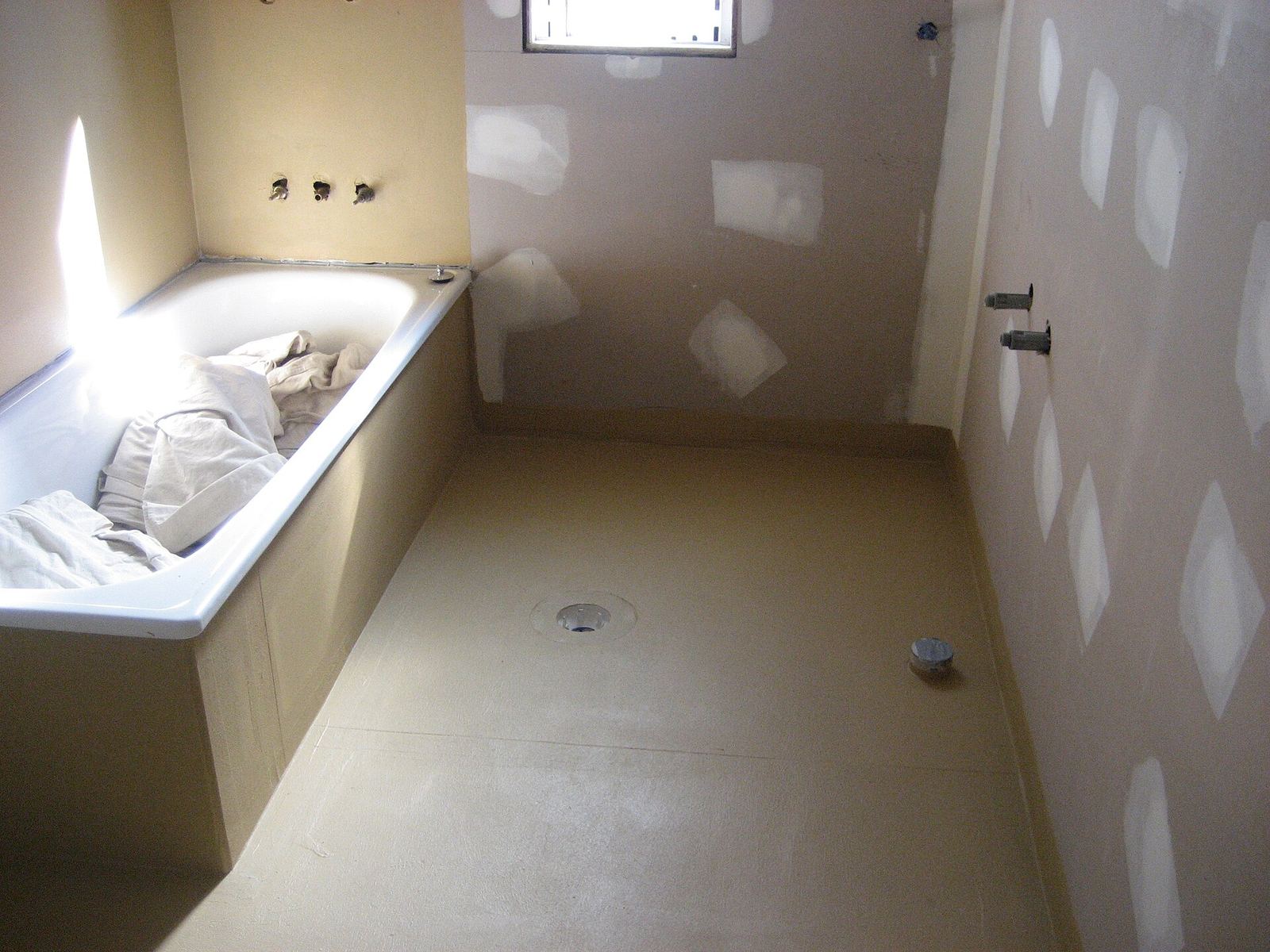 Badkamer in aanbouw met een waterdichtingslaag op de vloer en onderaan de wanden, rond de afvoer en het ingebouwde bad